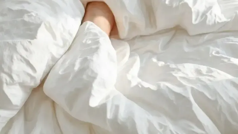 Pés sob lençóis macios e fofos em uma cama de casal, simbolizando conforto e descanso.
